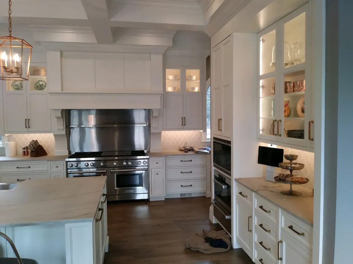 Bright white kitchen with stainless steel stove, island, and glass-front cabinets; hardwood floors.