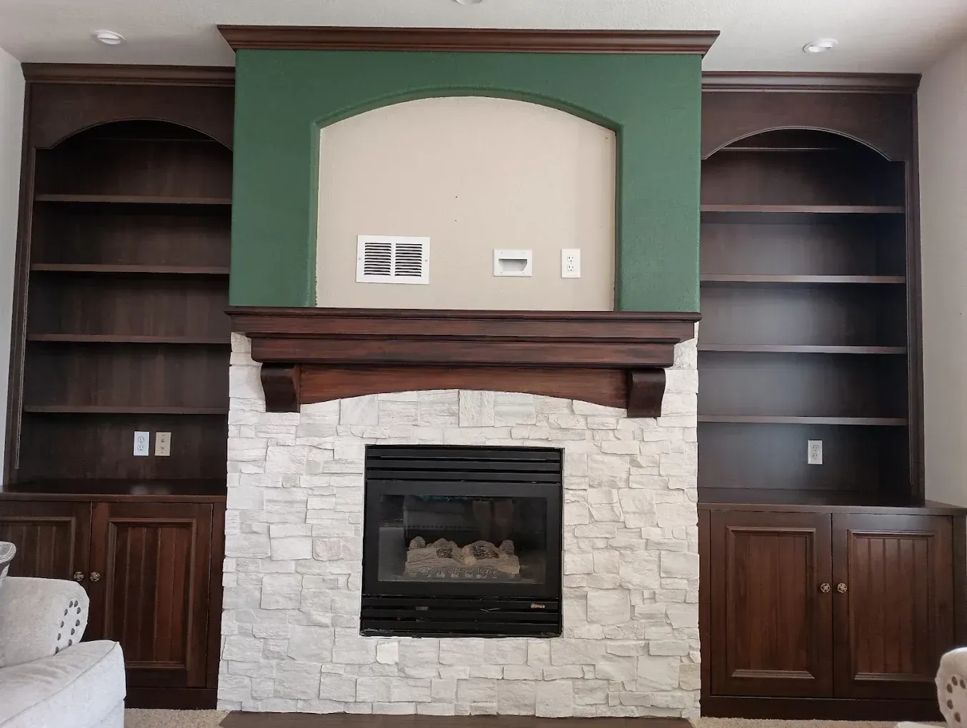 Living room built-in shelves framing a white stone fireplace with dark wood cabinets and green accent trim