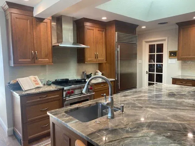 Modern kitchen with wooden cabinets, stainless stove, and marble island countertop with sink and faucet