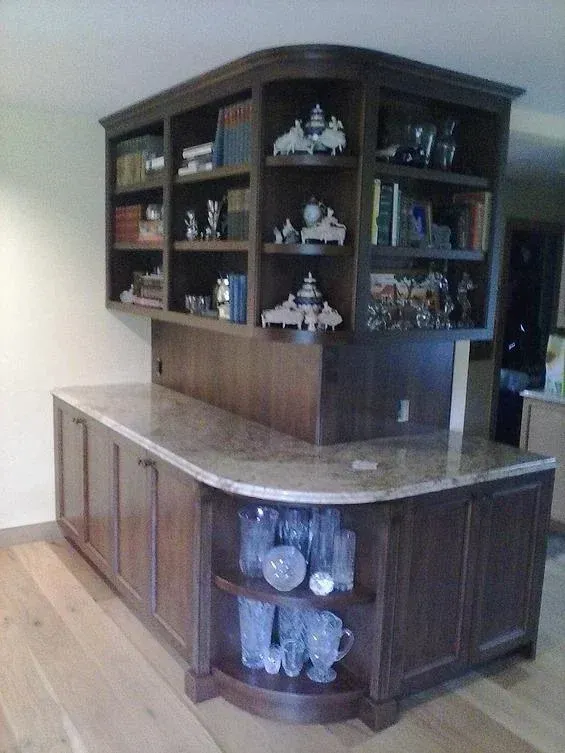 Dark wood bar cabinet with marble countertop and built-in shelves in a home interior