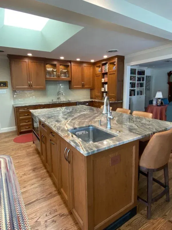Kitchen with wood cabinets, marble island, and stainless sink under a skylight.