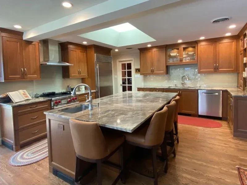 Spacious modern kitchen with wooden cabinets, large marble island, and stainless steel appliances.