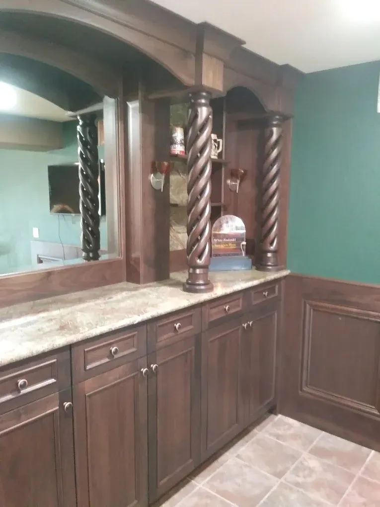 Dark wood bar cabinet with carved columns, mirror, and green walls in a tiled room