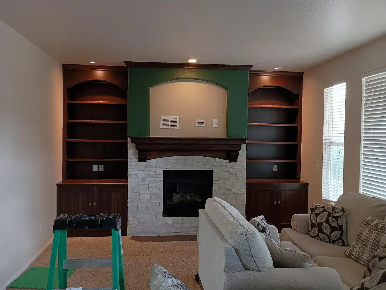 Living room with fireplace, built-in shelves, and beige sofas facing a green accent wall