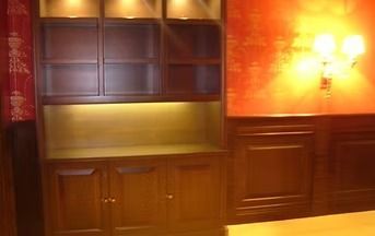 Dark wooden cabinet with upper shelves, lower cabinets, and warm lighting against a red and brown wall.