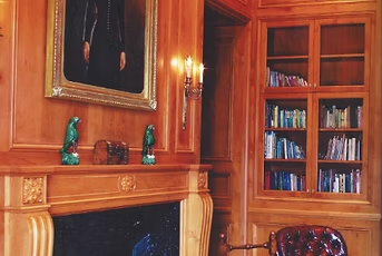 Wood-paneled library with fireplace, bookshelves, and art, featuring a painting and decorative elements.