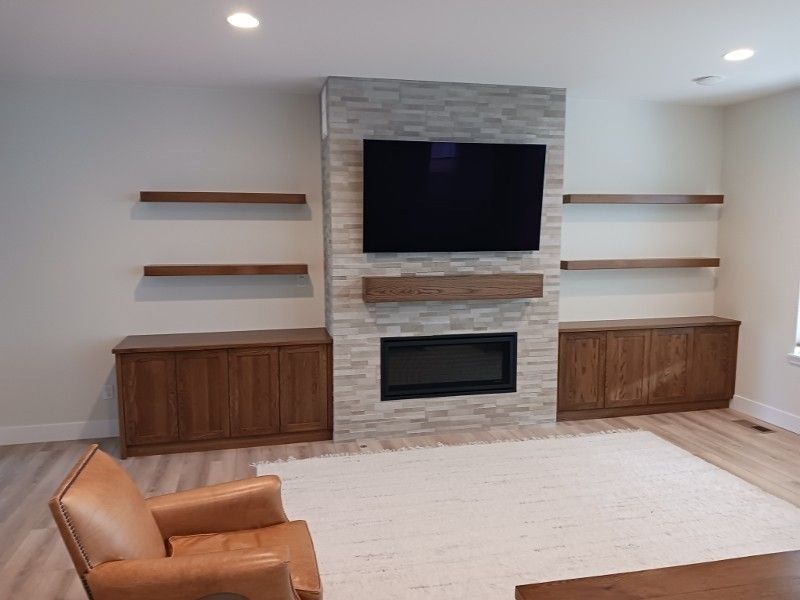Living room with fireplace, TV, floating shelves, and cabinets. Includes an armchair and rug.