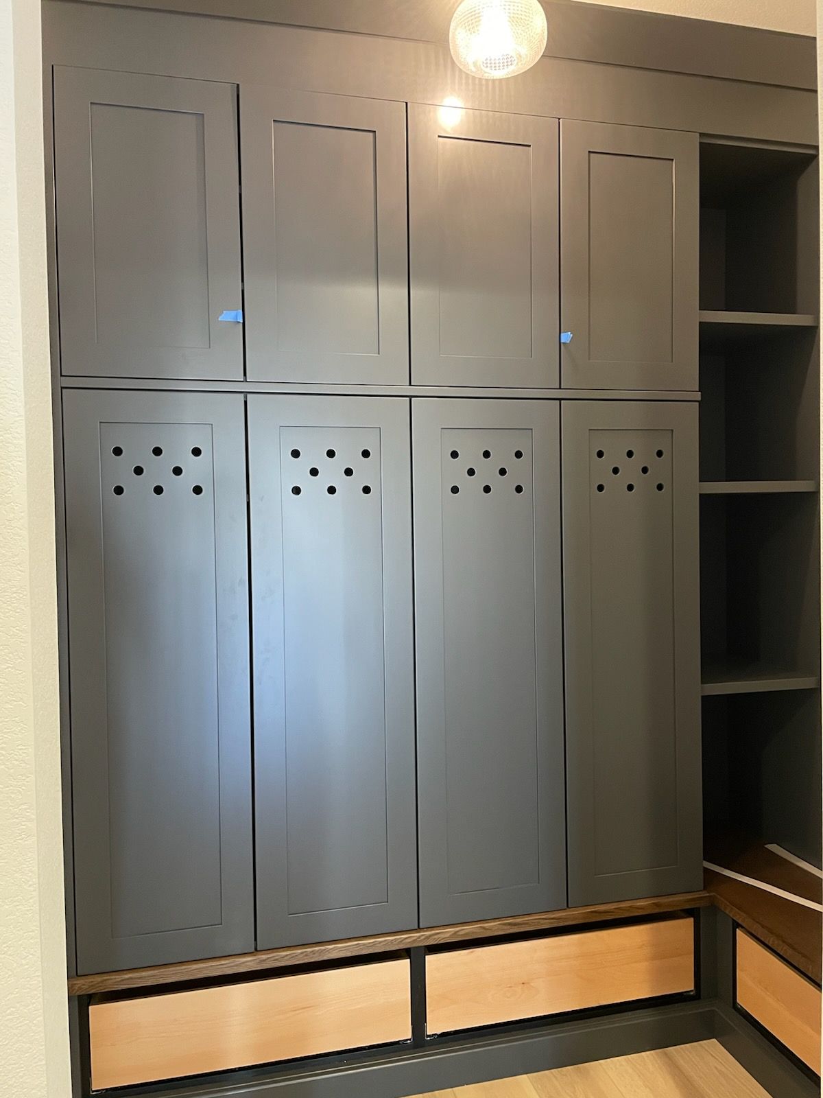 Gray built-in locker wall with cabinet doors, open shelves, and two wooden drawers at the bottom.