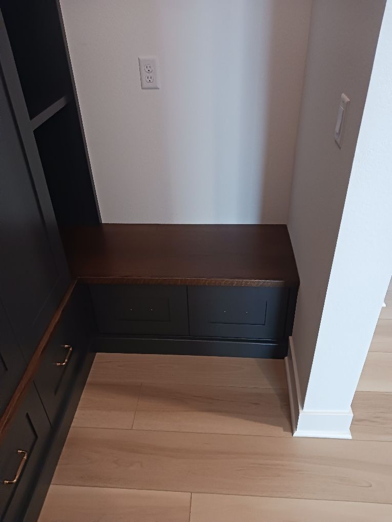 Built-in dark wood bench with drawers in a small closet nook with light wood floor and white walls