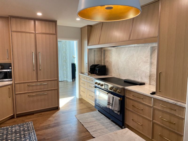 Modern kitchen with wood cabinets, stainless oven, and a large orange pendant light over a central island.