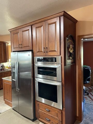 Kitchen cabinet wall with stainless steel refrigerator and built-in oven, finished in medium wood tone