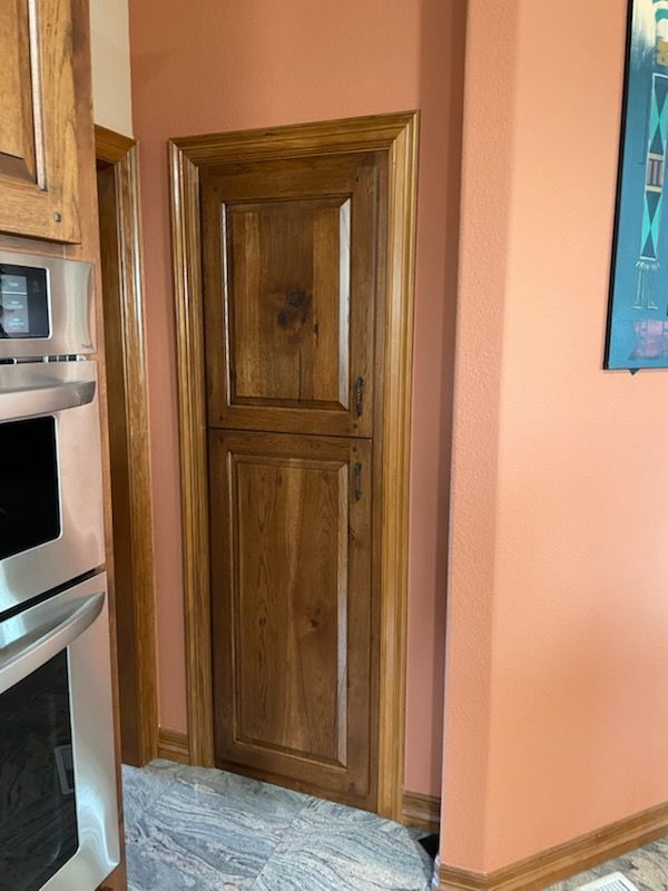 Kitchen with wood cabinets, built-in stainless oven, and a wood pantry door beside a peach wall.