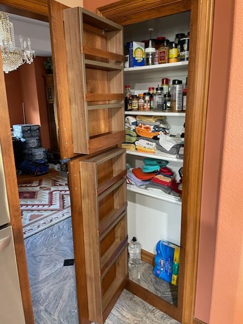 Open pantry cabinet with shelves of jars, cans, snacks, and household items in a home hallway.