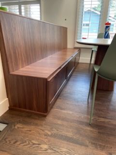 Wood-paneled waiting area bench with high back and built-in storage, beside a window in a room with wood flooring