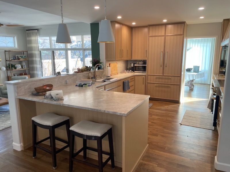 Bright modern kitchen with large island, wood cabinets, pendant lights, and two stools