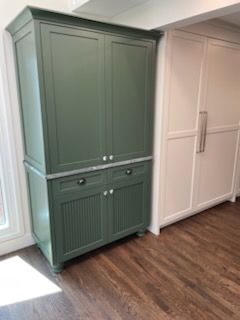 Green built-in cabinet with drawers and cabinet doors beside a white sliding door in a room with wood flooring