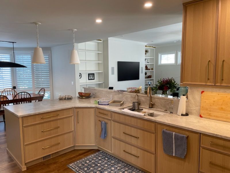 Bright, modern kitchen with wood cabinets, granite counters, pendant lights, and a wall-mounted TV in the background.