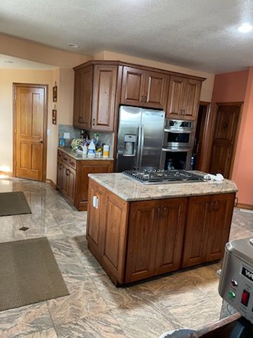 Kitchen with wooden cabinets, stainless steel refrigerator, and a central island on tile flooring.