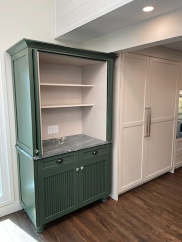 Green built-in cabinet with open shelves and drawers beside white closet doors in a bright room