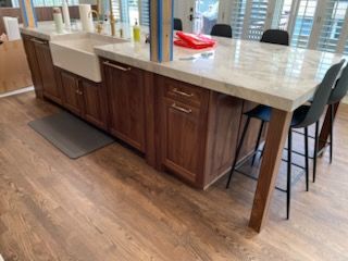 Kitchen island with wood cabinets, light countertop, and black stools in a bright open room