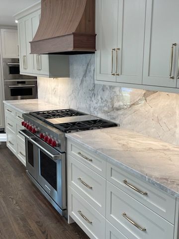 Modern white kitchen with marble countertops, gas range, copper hood, and built-in oven