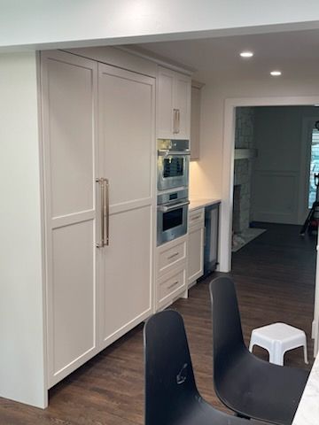 Modern kitchen with tall white cabinets, built-in ovens, and black chairs in the foreground.