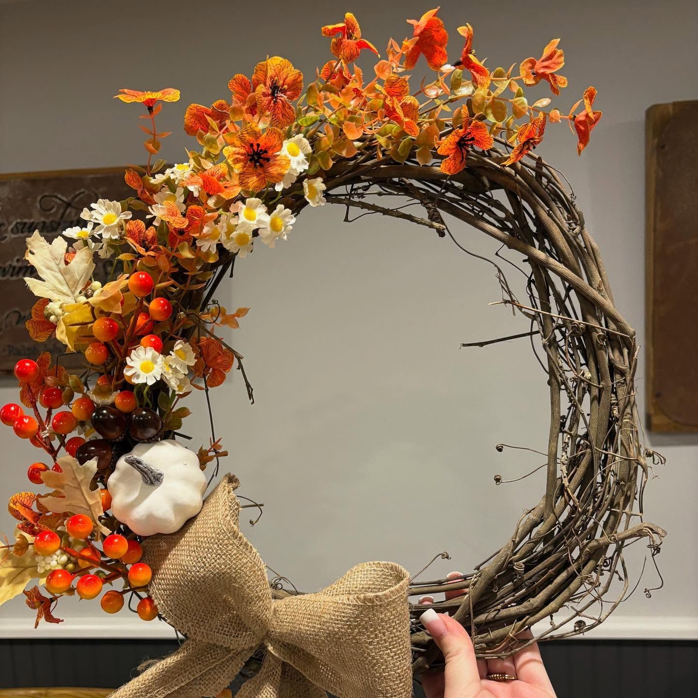 Fall wreath with orange and white flowers, berries, and burlap bow on a twig ring