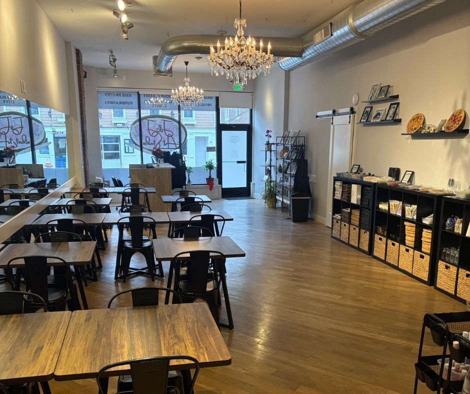 Empty modern café with wooden tables, black stools, chandeliers, and large front windows.