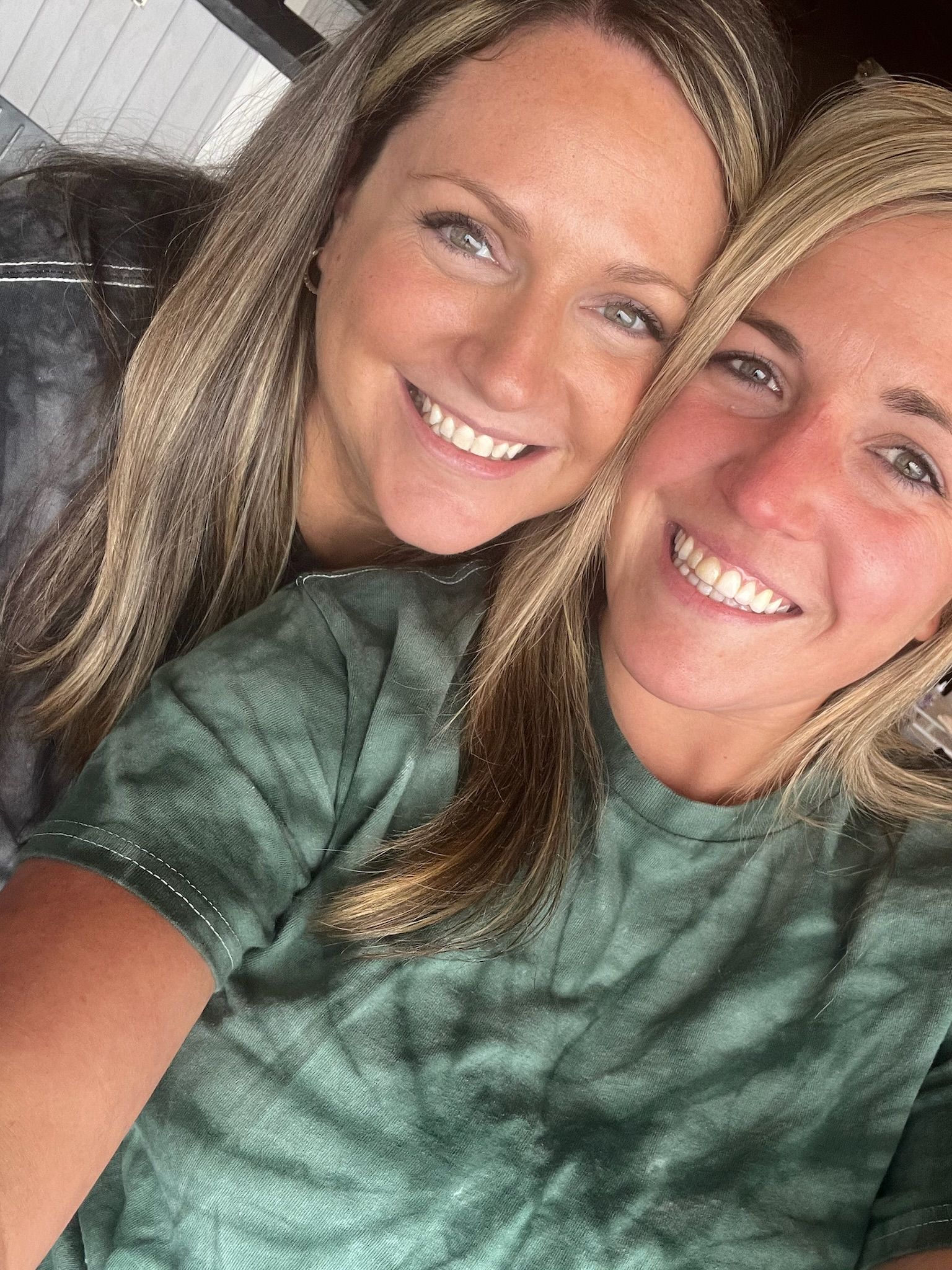Two smiling people in green shirts leaning close together for a selfie