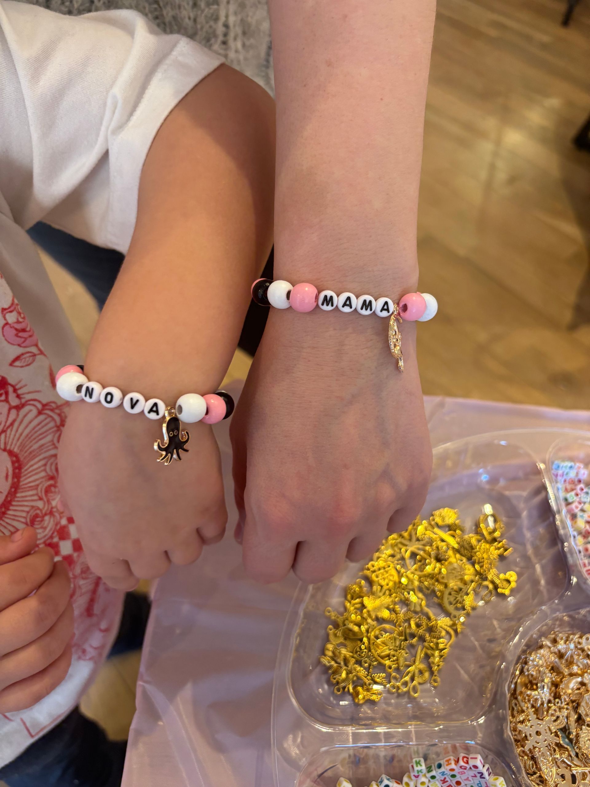Two people wearing matching beaded bracelets over a tray of colorful beads at a craft table
