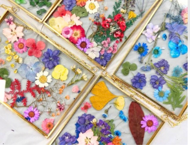 Four floral resin coasters with pressed flowers in pink, purple, yellow, and blue arranged in a diamond pattern