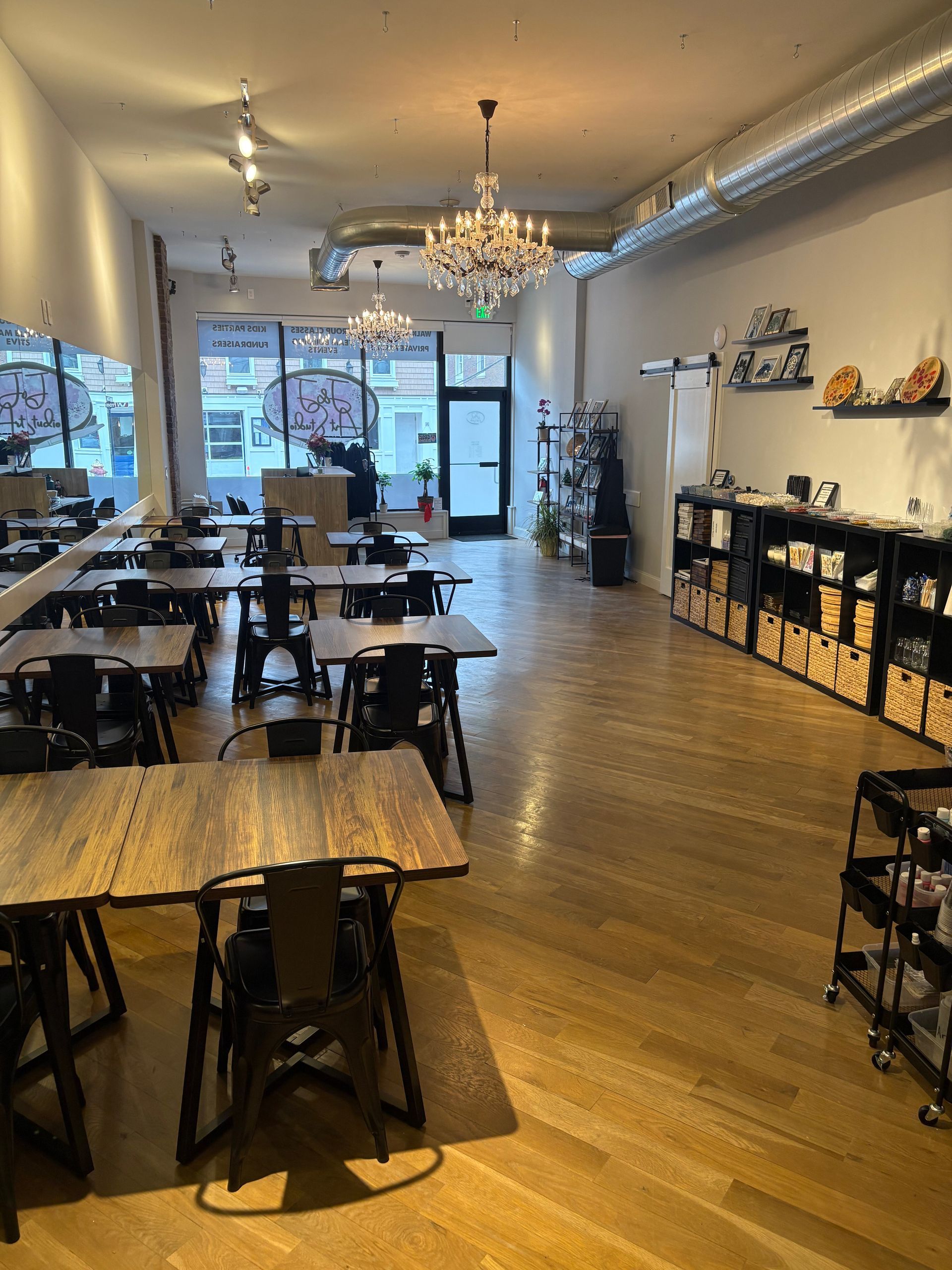 Empty modern café interior with wooden tables, black chairs, chandeliers, and large front windows