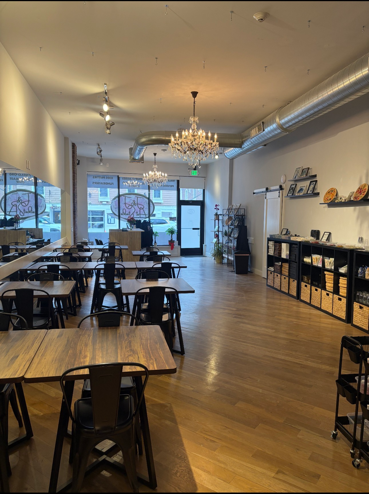 Bright café interior with wooden tables, chairs, chandelier, and large front windows.