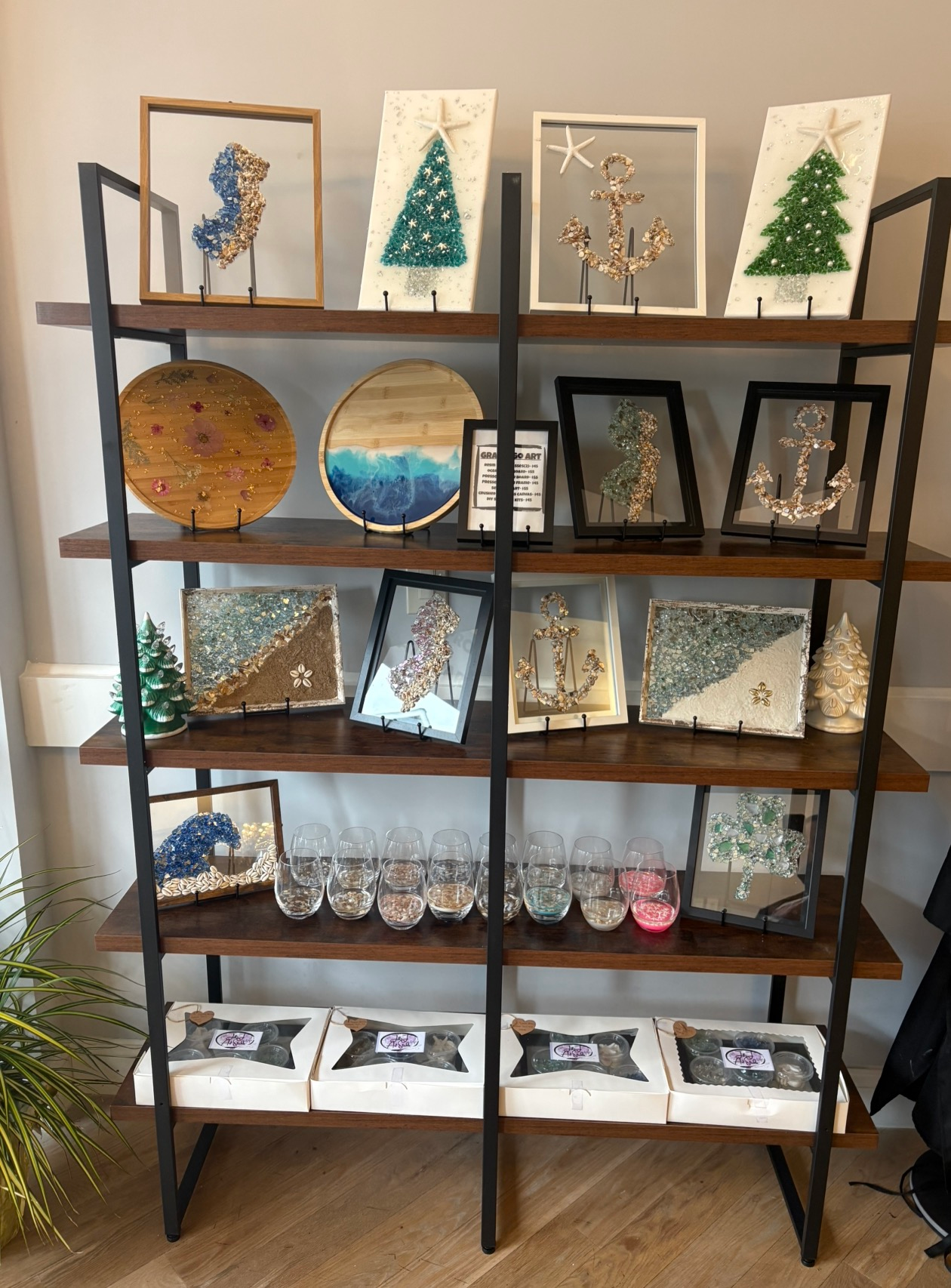Wood shelf display of holiday art and decorations, including trees, framed ornaments, mugs, and glassware