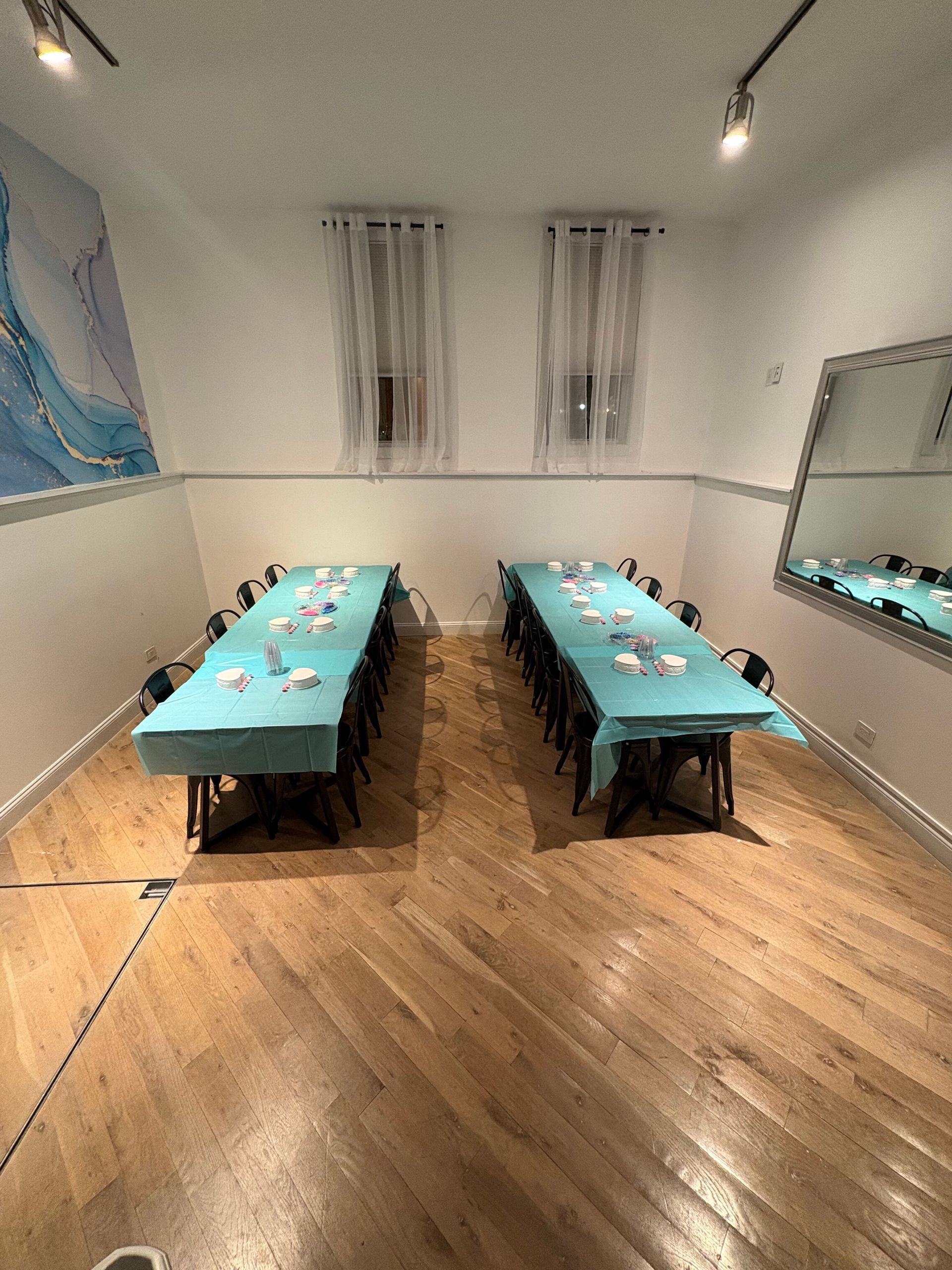 Small meeting room with two long turquoise-covered tables and chairs on a wood floor.