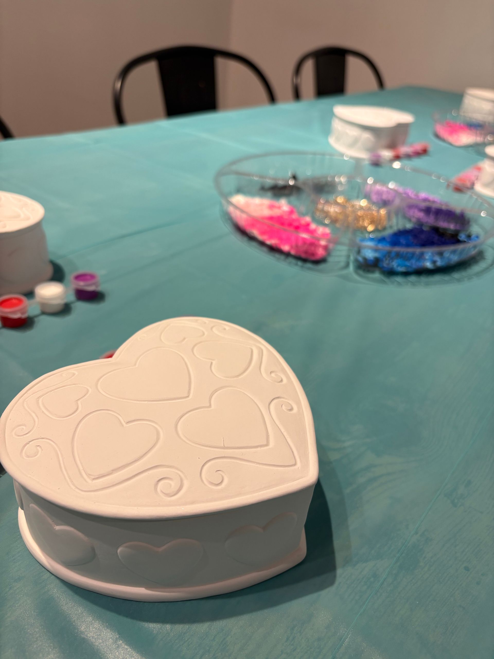 White heart-shaped keepsake box on a table with colorful craft beads and supplies in the background
