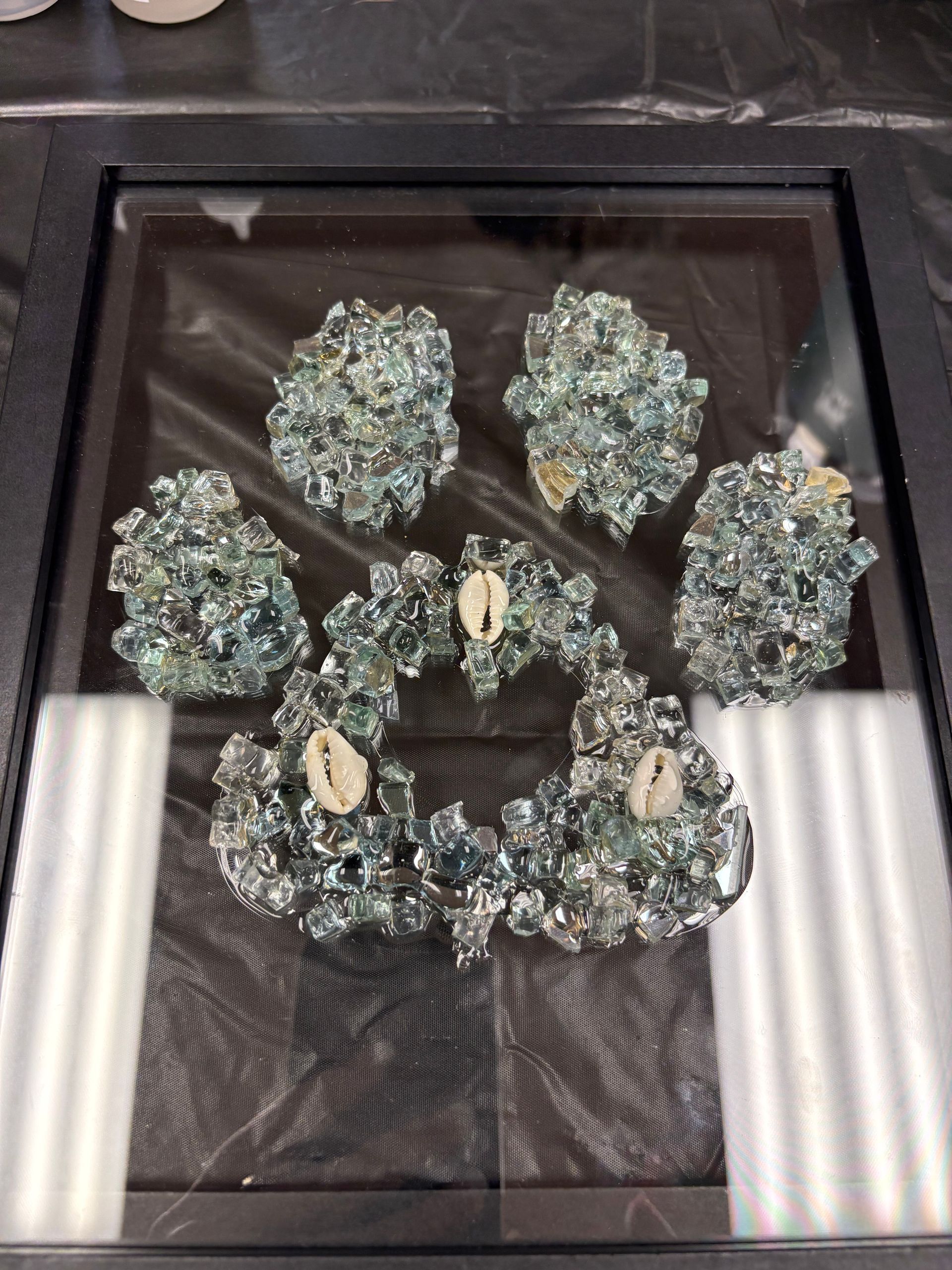 Framed display of a beaded, blue-green paw print on a black background