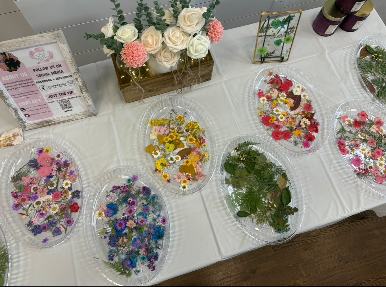Flower petals and small craft items arranged in clear bowls on a white table beside a floral centerpiece.