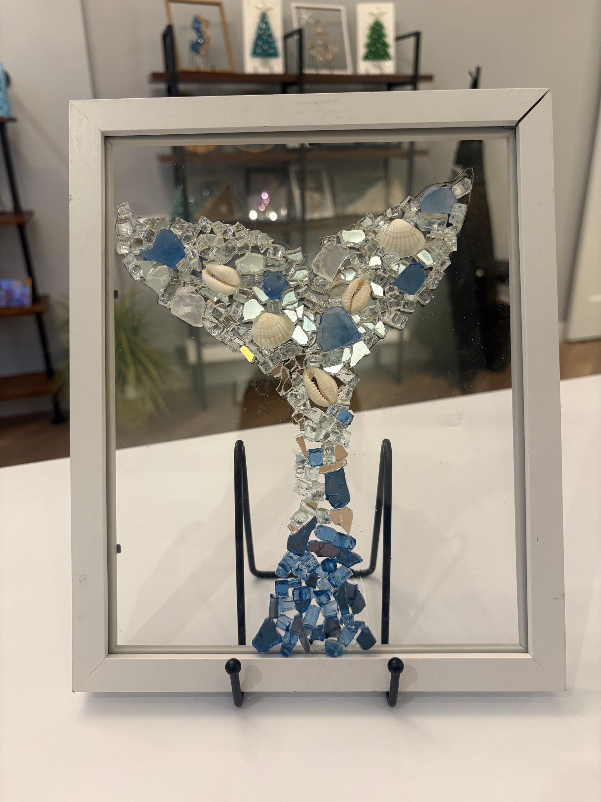 Abstract blue-and-white mosaic sculpture displayed in a white frame on a stand
