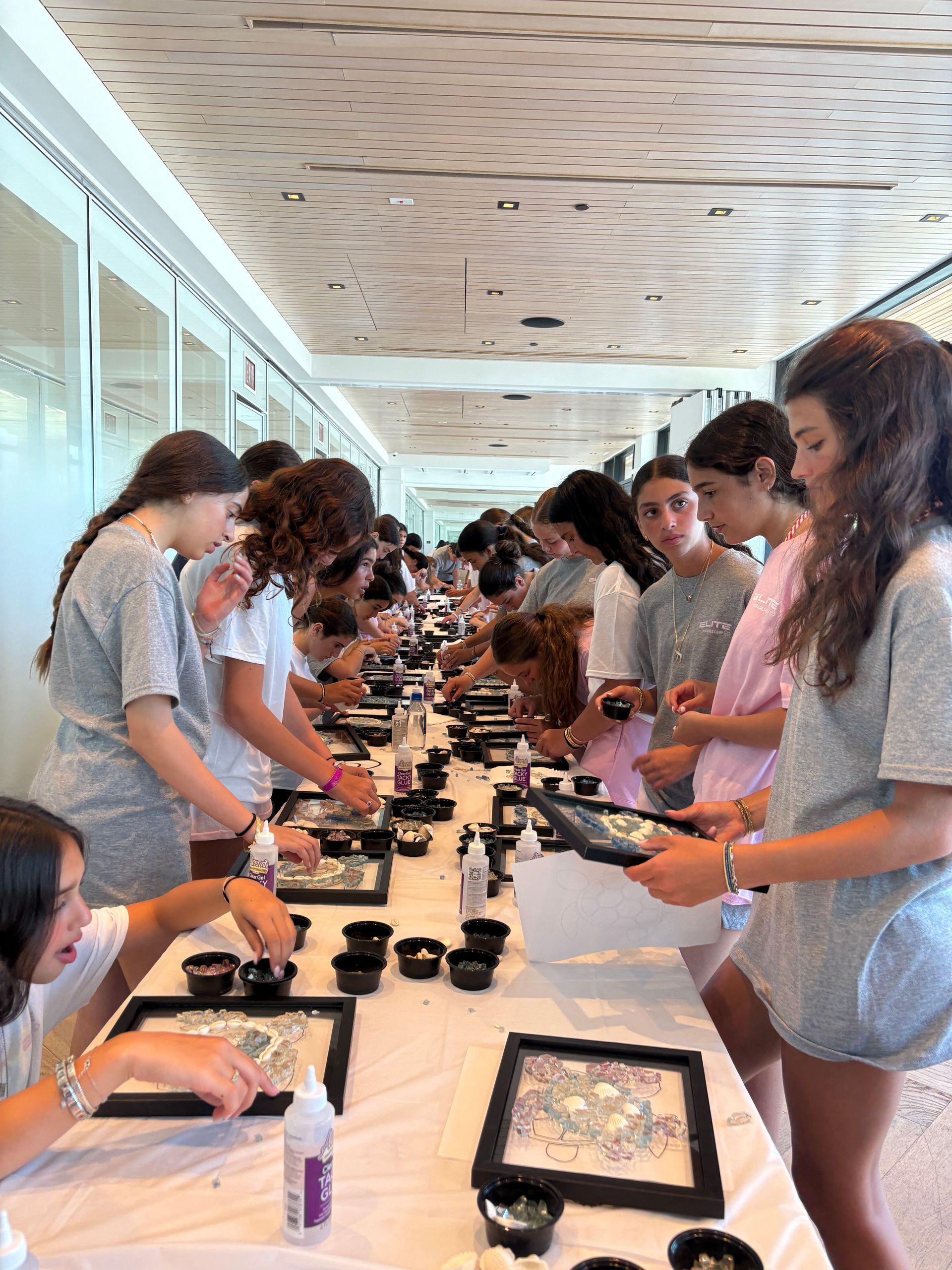 Students line a long table, arranging makeup products in a bright room.