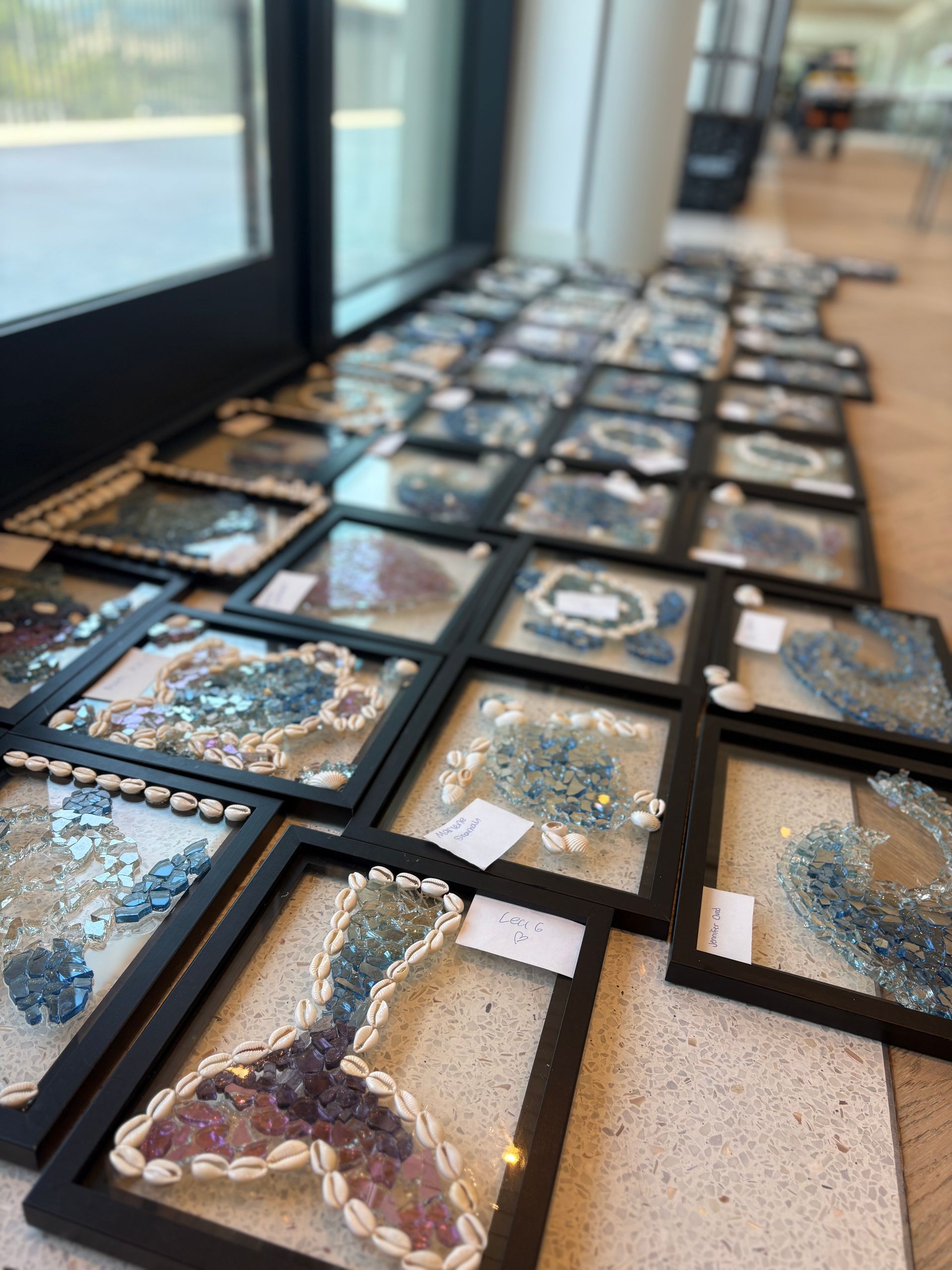 Framed resin art pieces with dried flowers arranged on a floor beside large windows