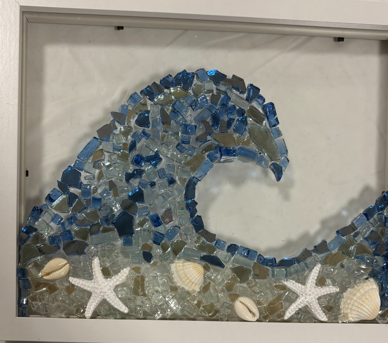 Blue glass wave mosaic with white seashells on a sandy base in a framed display