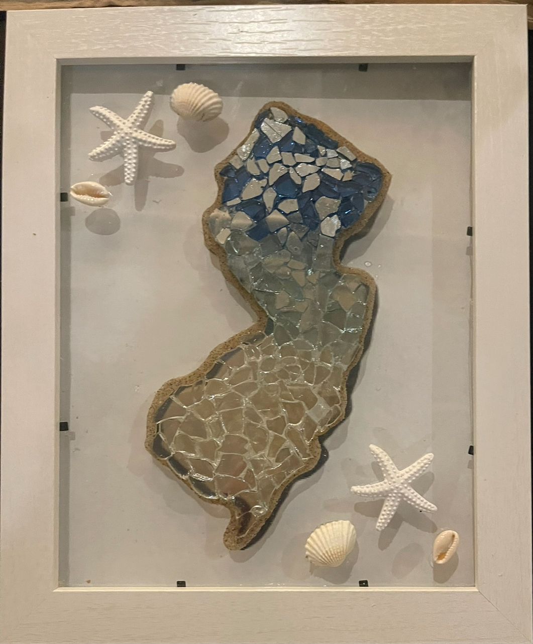 Framed seashell mosaic in blue and tan with starfish and shells on a white background