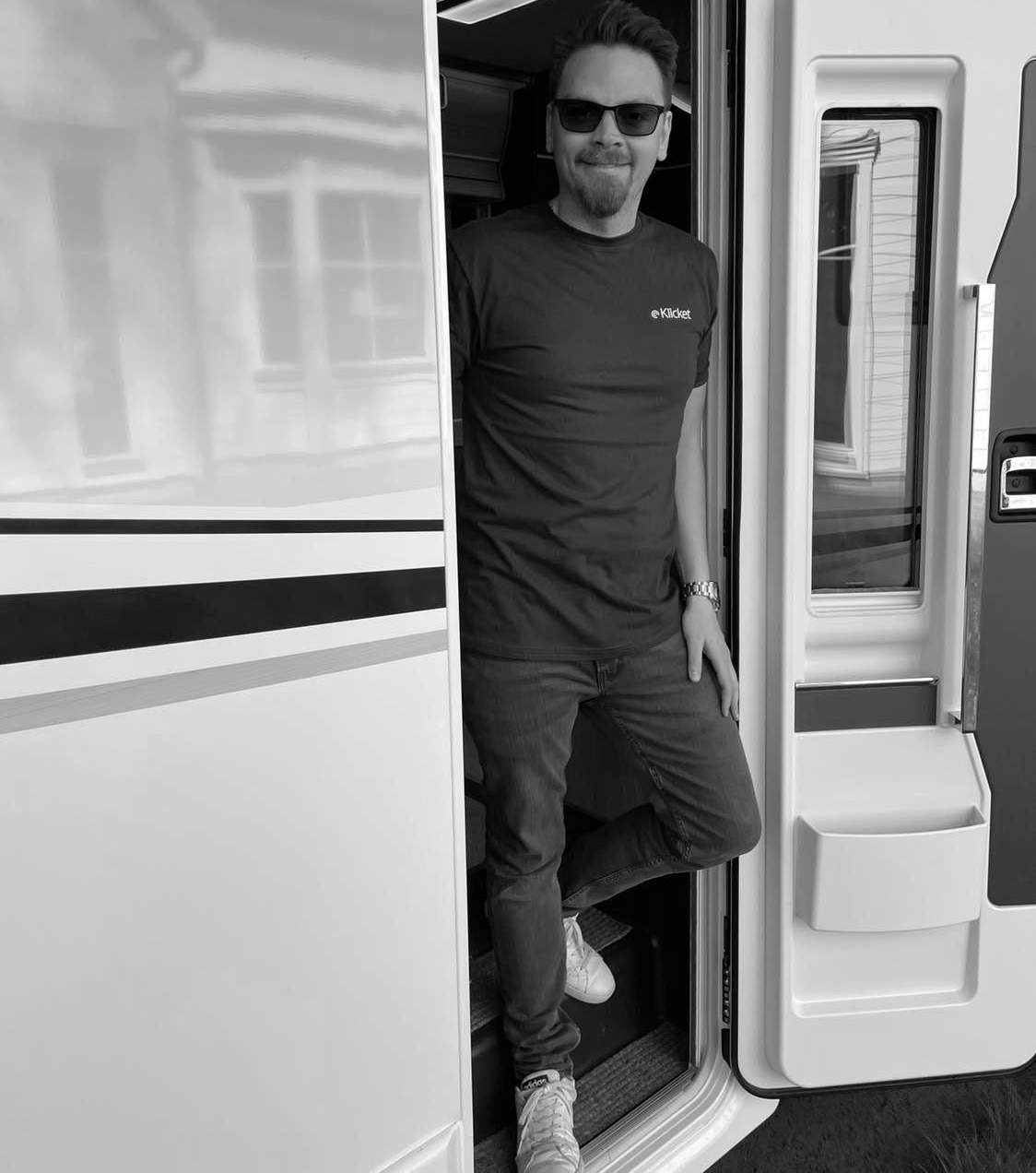Man wearing sunglasses and a t-shirt, stepping out of a recreational vehicle doorway.