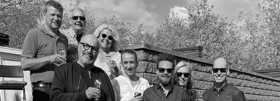 Group of people smiling, holding drinks, outdoors on a sunny day. Black and white photo.