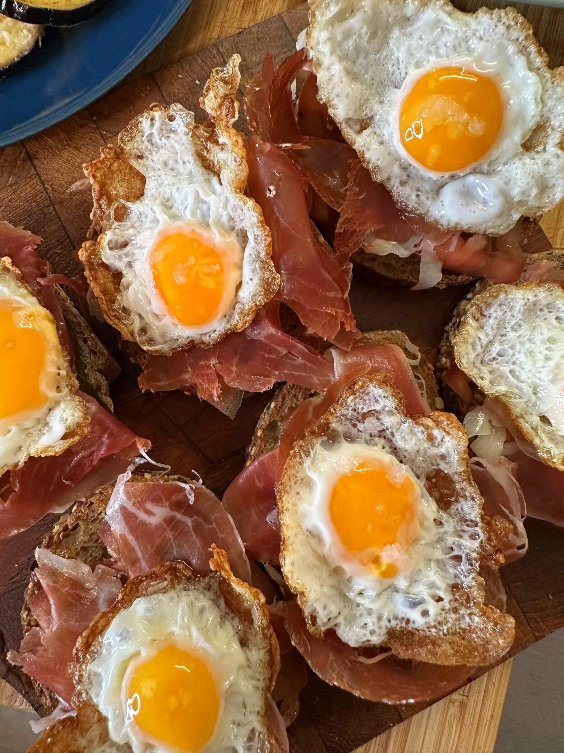 Un montón de huevos sobre tostadas con jamón sobre una mesa de madera.