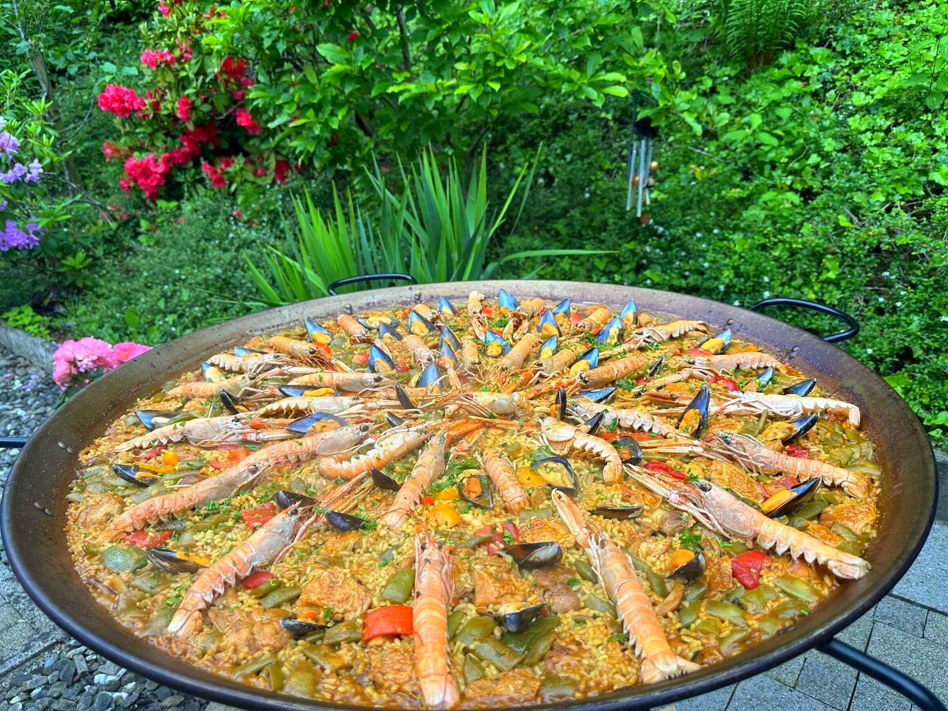 Una gran sartén con paella está sobre una mesa en un jardín en Suiza