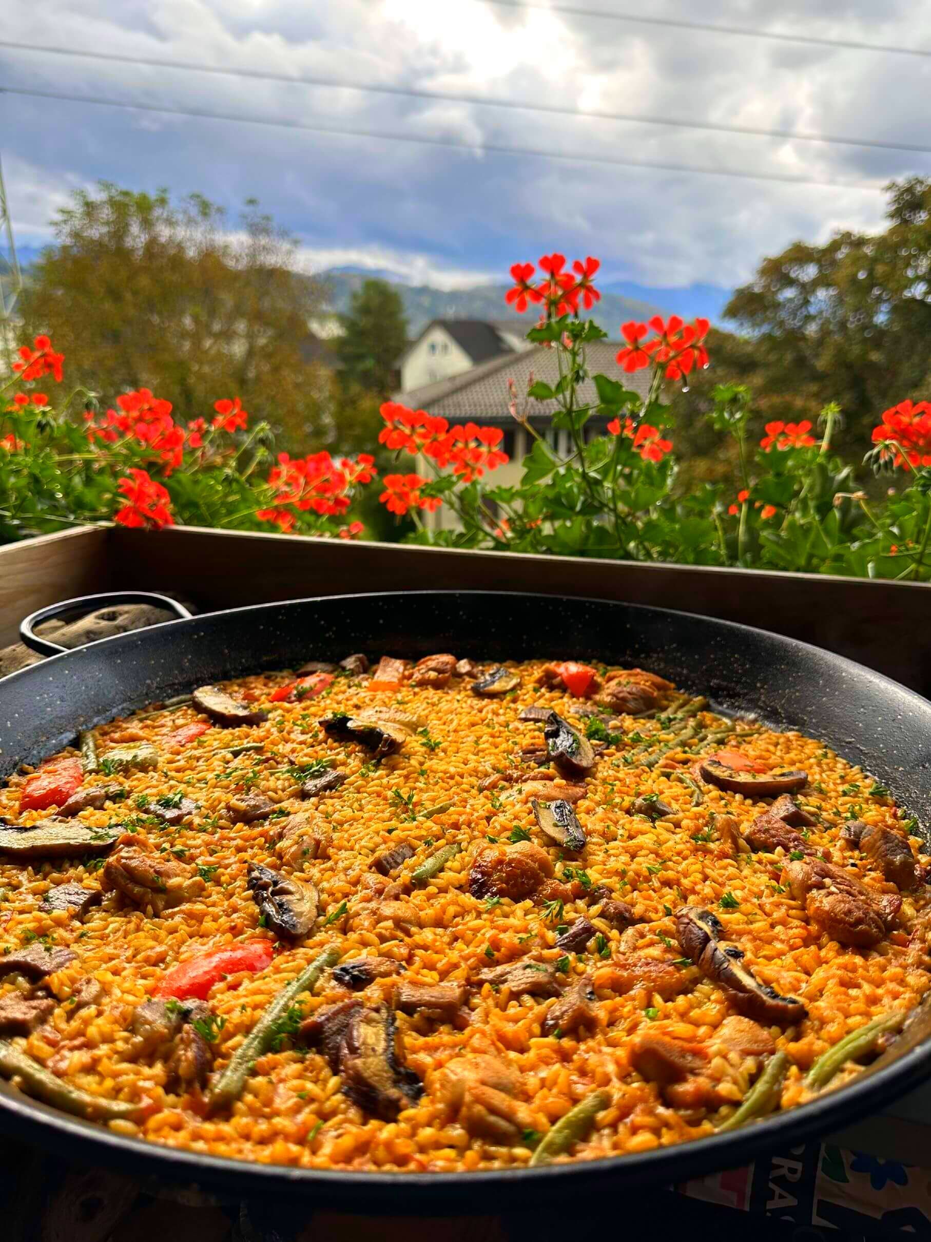 Una sartén con paella está sobre una mesa con flores al fondo en Suiza