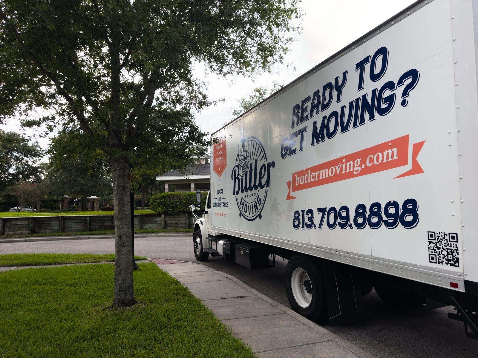 Moving truck parked beside a sidewalk in a leafy neighborhood, with bold “Ready to Move?” signage on the side.