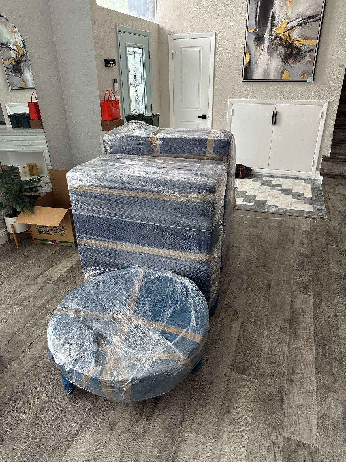 Living room with furniture wrapped in plastic for moving or delivery, including a chair and ottoman.